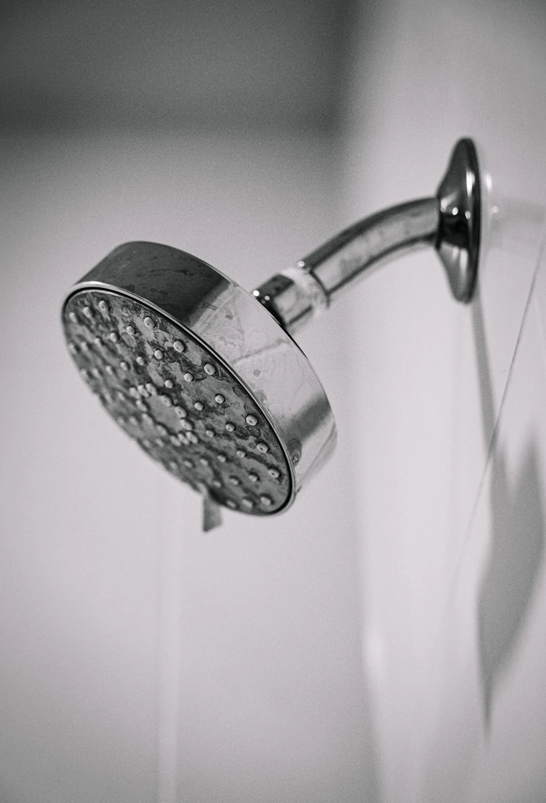 Black and white photo of a sleek, metal showerhead mounted on a bathroom wall