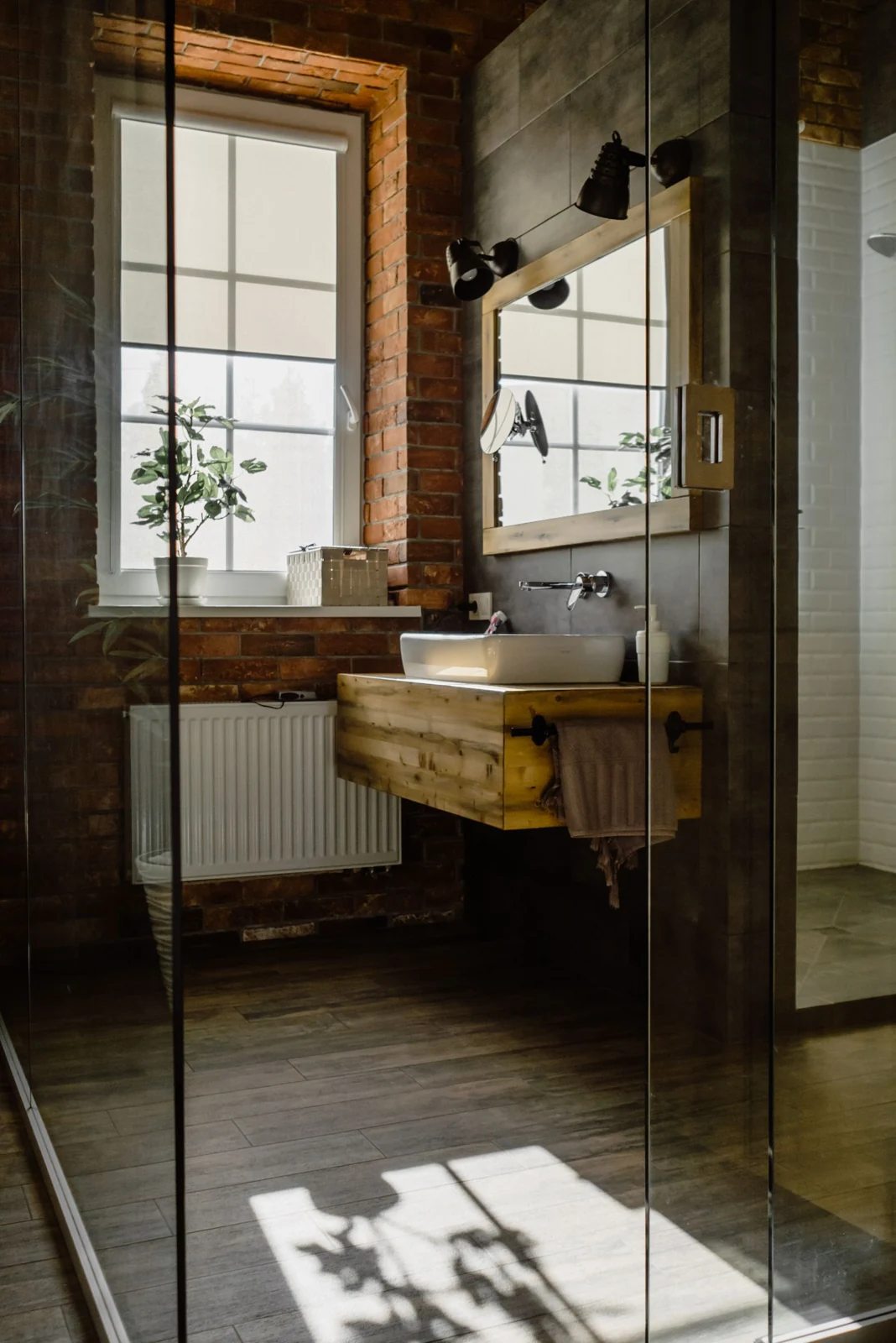 Modern bathroom with glass door, wooden sink, and natural brick wall