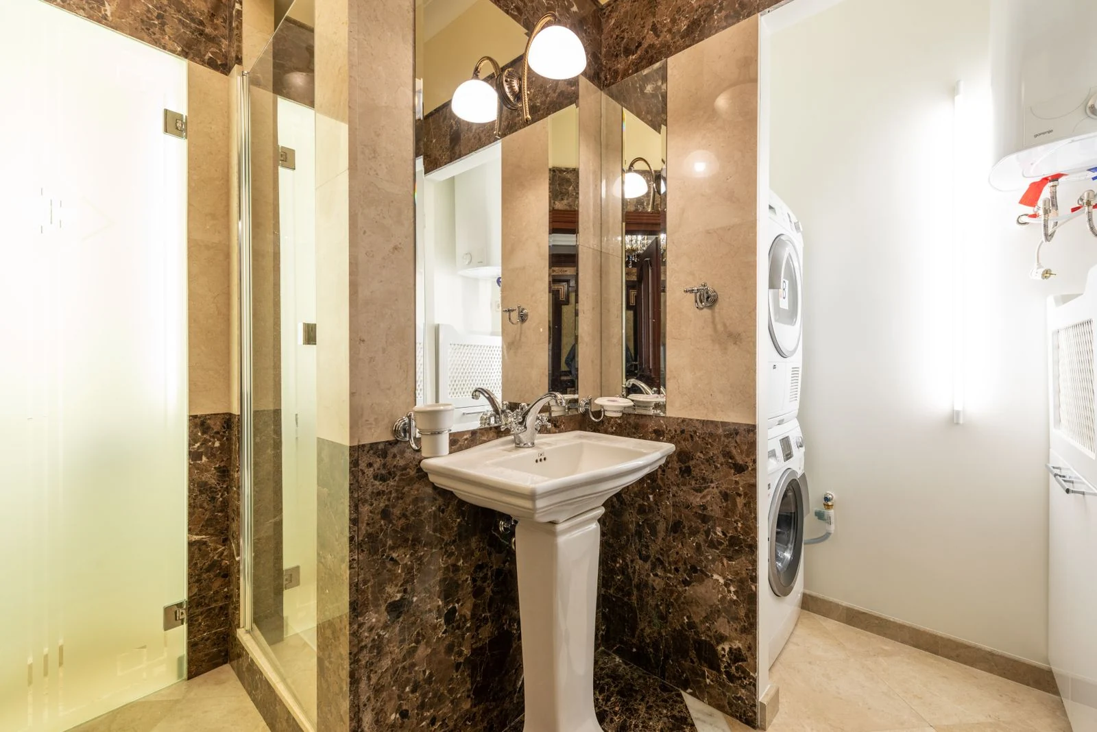Elegant bathroom interior featuring marble walls, a pedestal sink, and a washer-dryer unit
